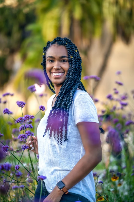 the smiling girl is standing in purple flowers