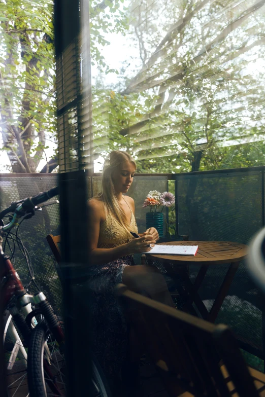 a woman sits on the bench next to her bike and writes on her paper