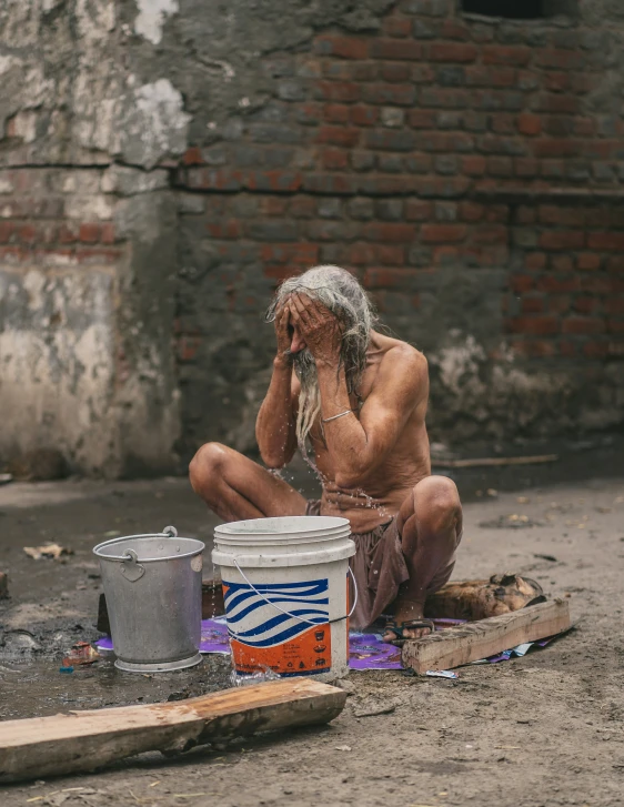 man with a silver hair is sitting on the ground next to buckets