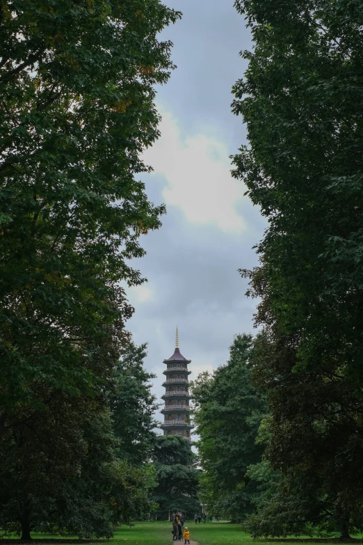 people walking in a grassy area with trees and a pagoda tower behind them