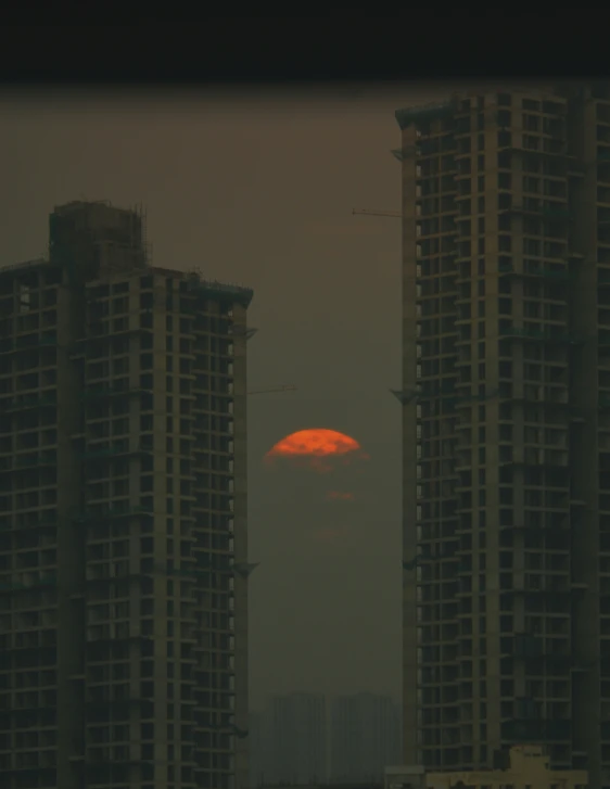 a red and yellow moon is in the distance between two buildings