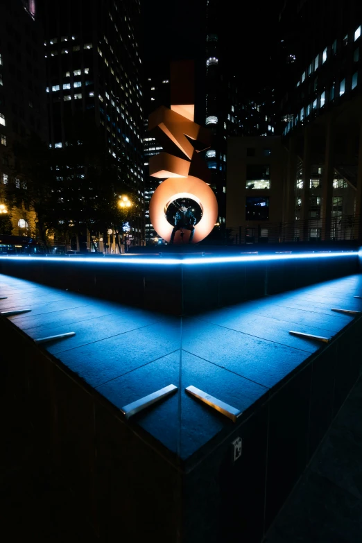 a blue lit sculpture with buildings in the background