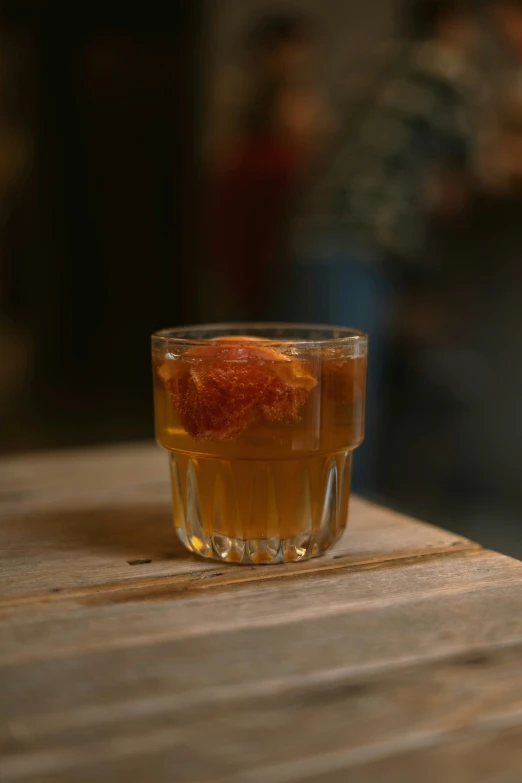 a glass of alcohol on a table with people watching