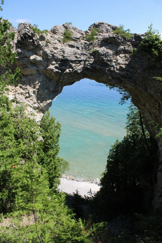 a stone arch over the water on a sandy beach