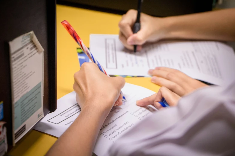 two people at a desk doing paperwork with pen and paper