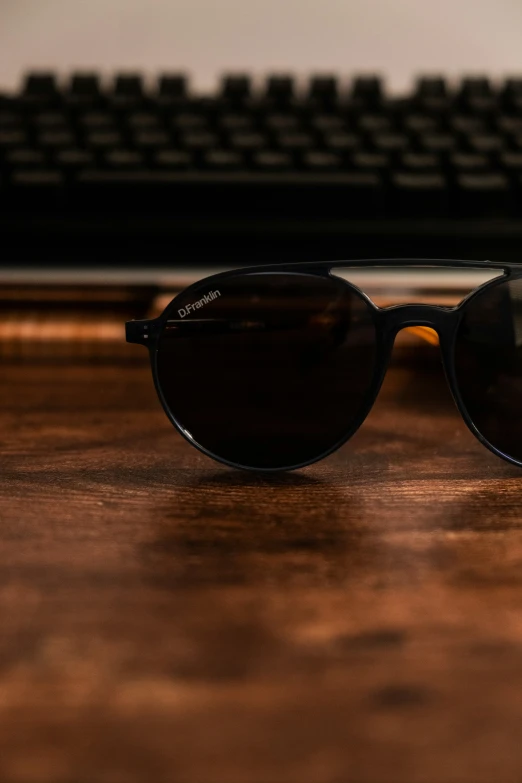 some sunglasses on a wood desk and some keyboard