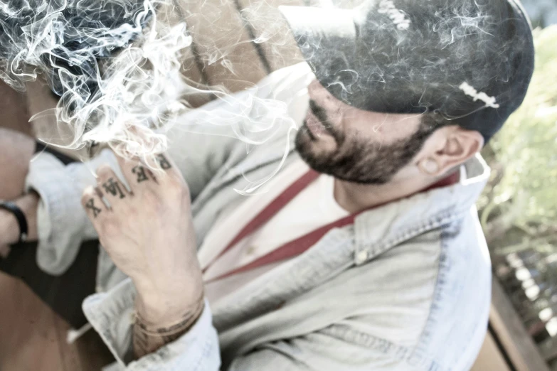 a man with a hat sitting down smoking a cigarette