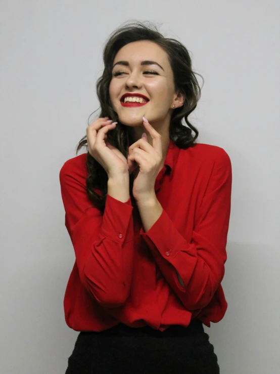 a woman in a red shirt smiling with her hands on her cheeks