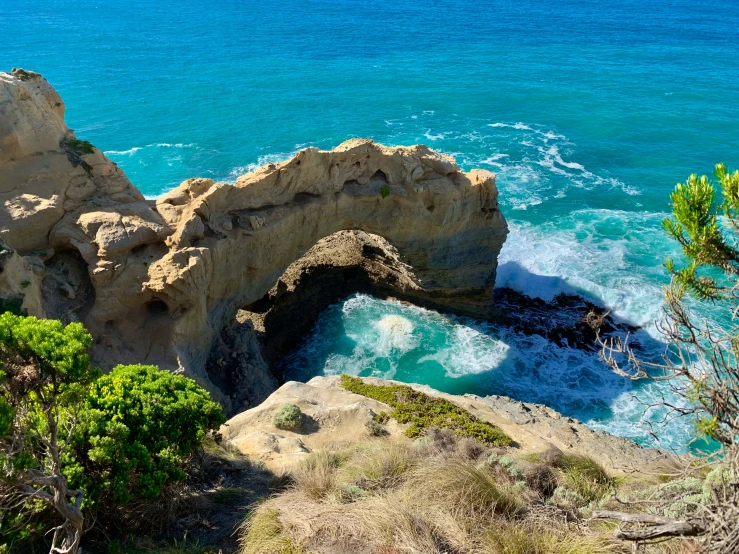 a sandy beach and large arch shaped rock formation with blue water