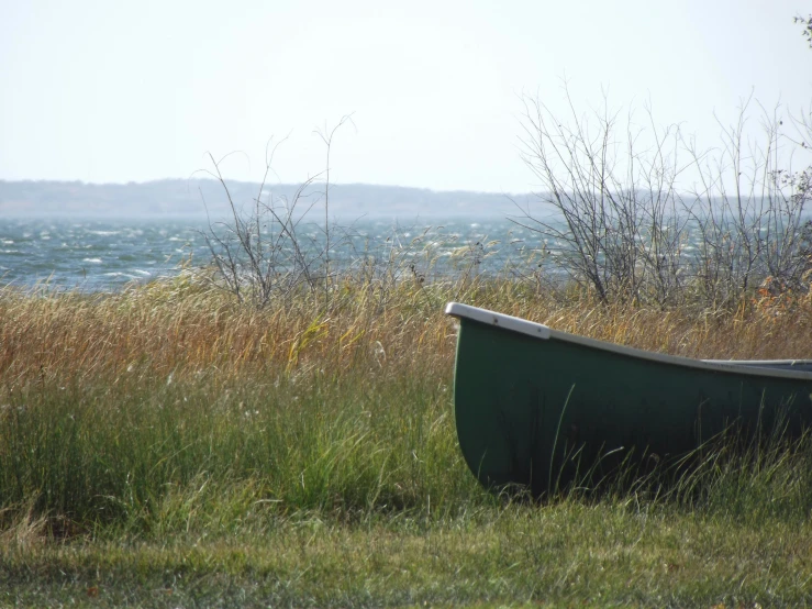 an empty green boat sitting on top of a grass covered field