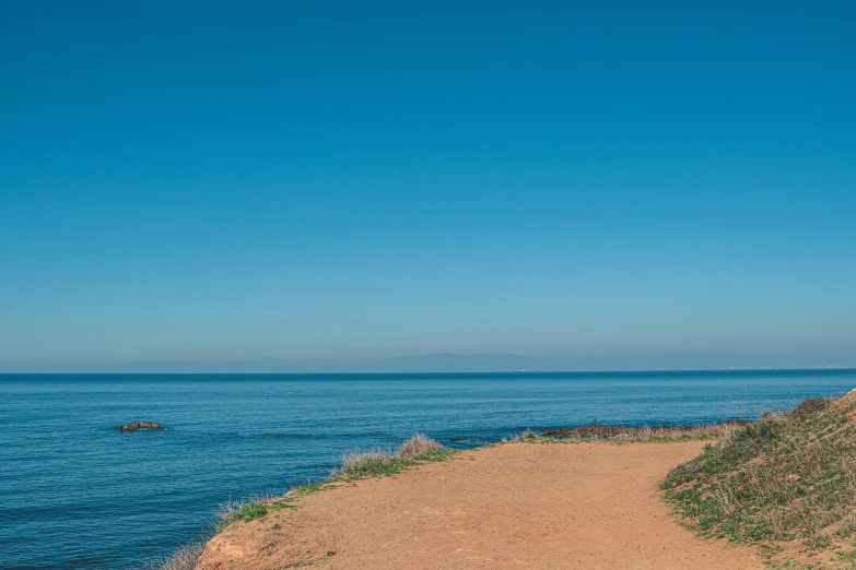 a view looking out to the ocean with a man sitting on the ledge