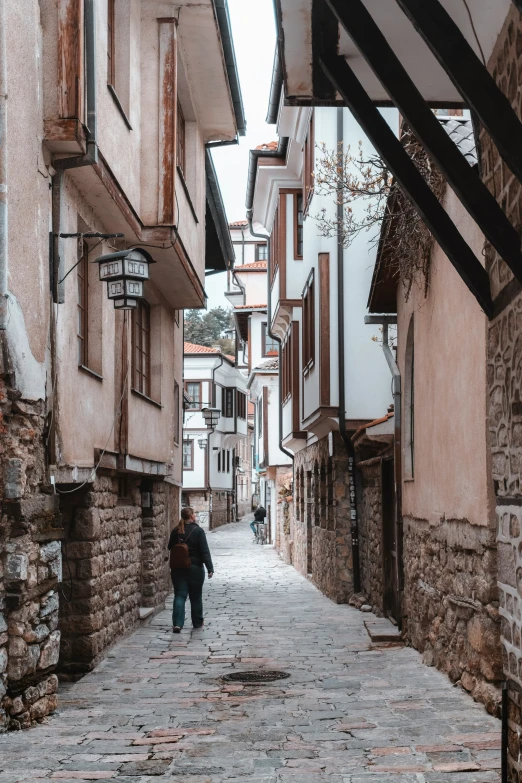 two people walking down a cobblestone street between buildings