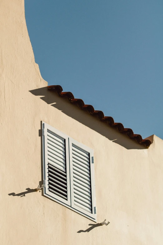the white wall of a building with a window and shutters is shown against a blue sky