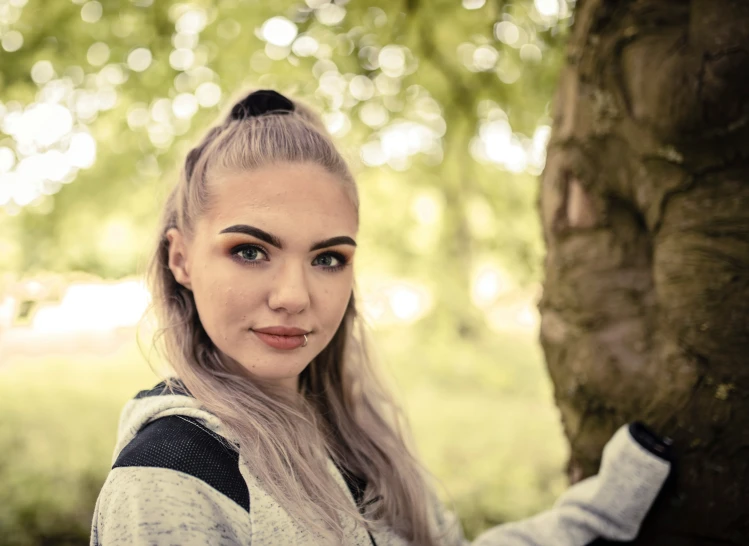 a girl is posing in front of a tree