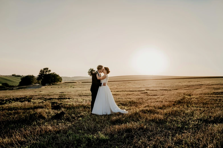 the newly married couple stand in the sundown field