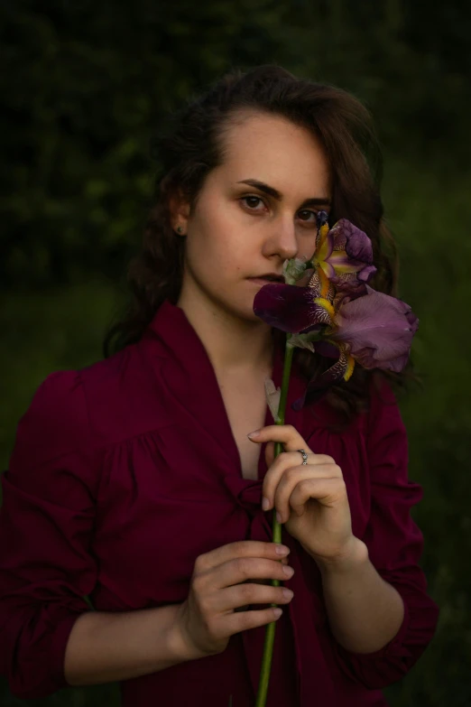 a woman standing outside holding a purple flower