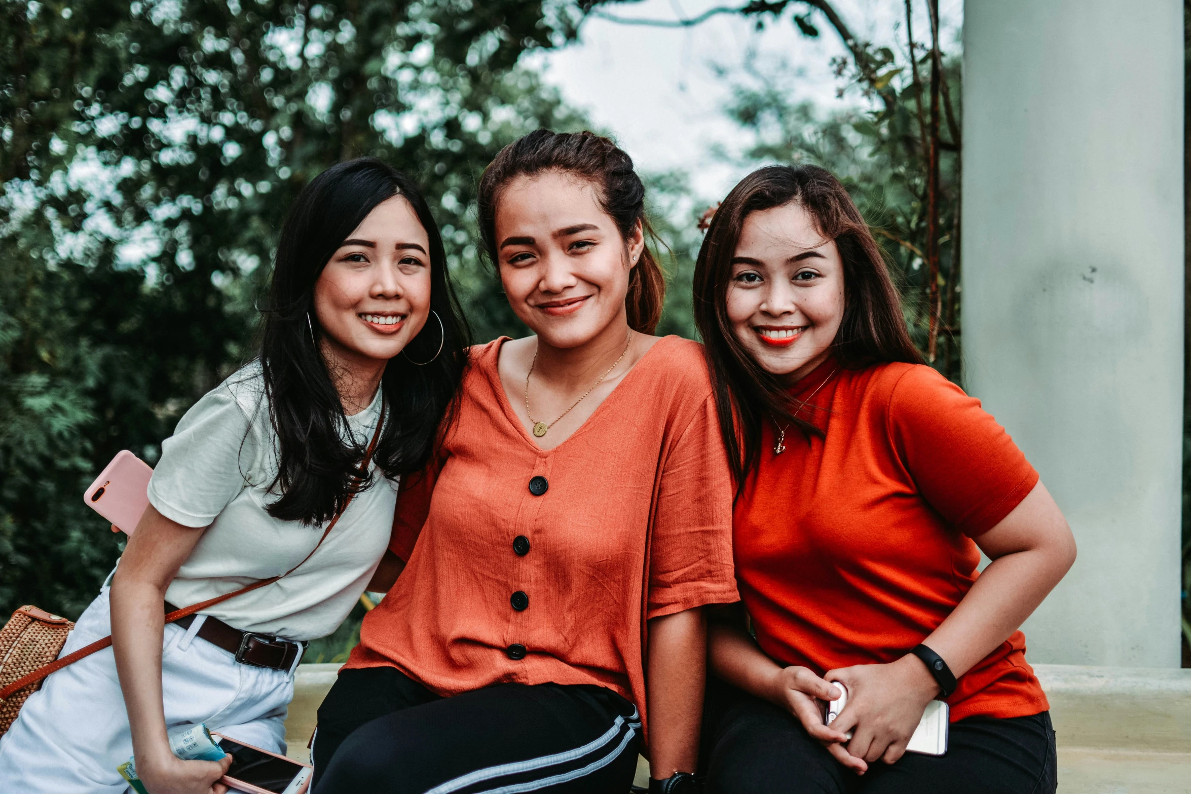 three girls are sitting on a bench smiling at the camera