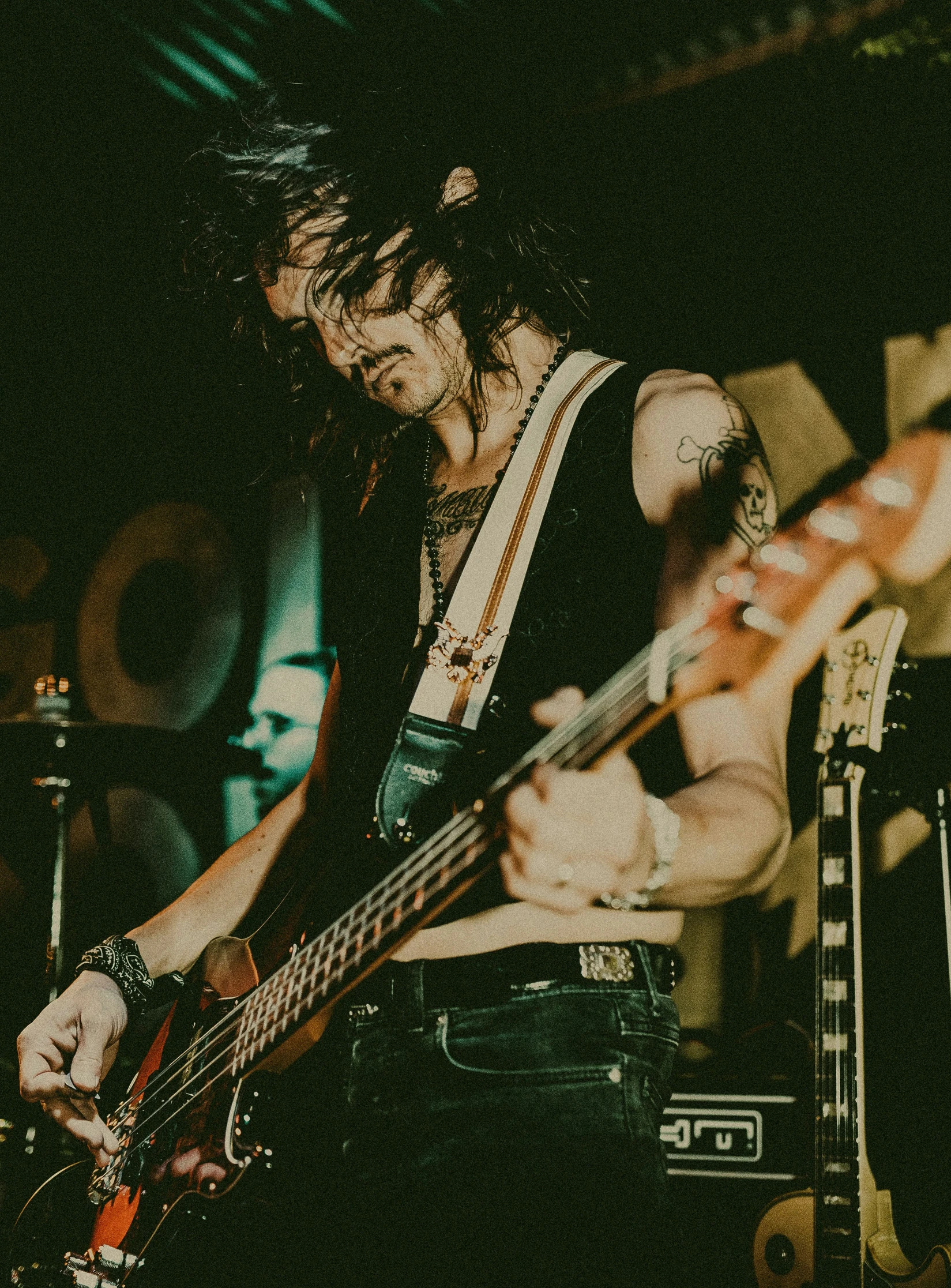 man with black and white shirt playing bass guitar in front of a speaker