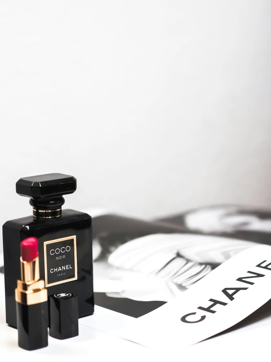 a black bottle of chanel no5, next to a white plate with a red lipstick