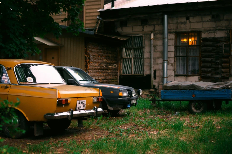 an old yellow car and trailer sitting in front of a building