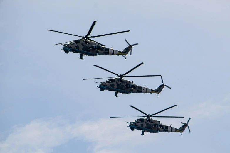 four military helicopters are flying overhead in the sky