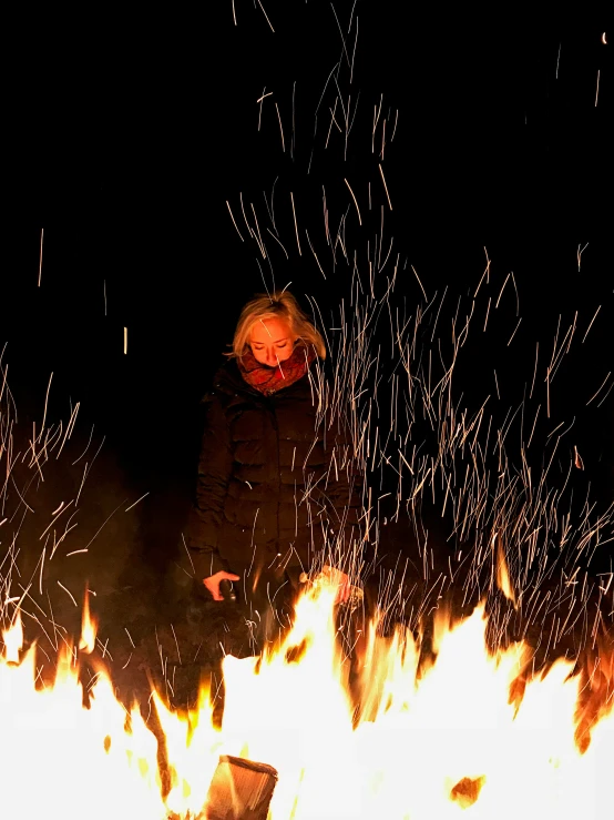 a woman sitting at the base of a huge bonfire