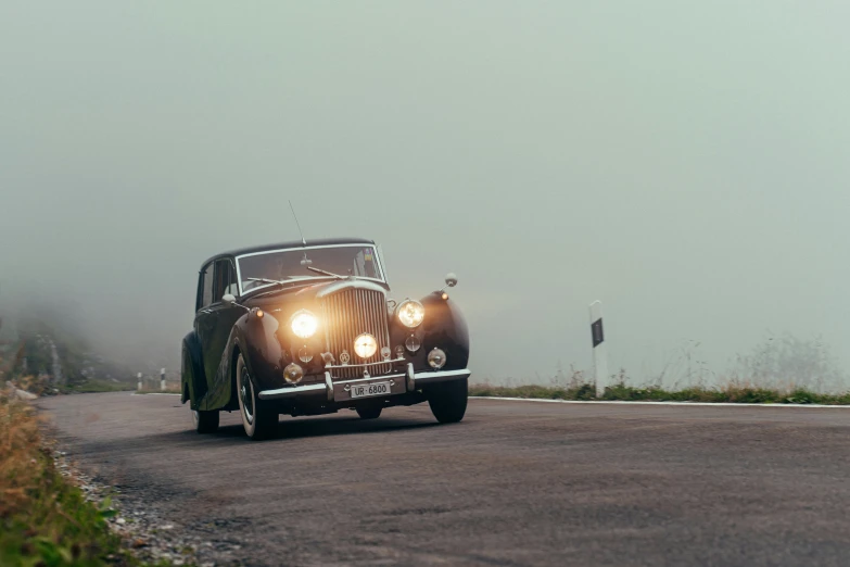 an old car in the fog driving down a road