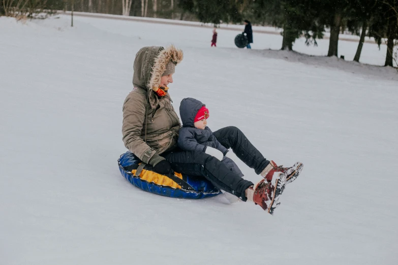 a woman and child riding a sled down a snow covered slope