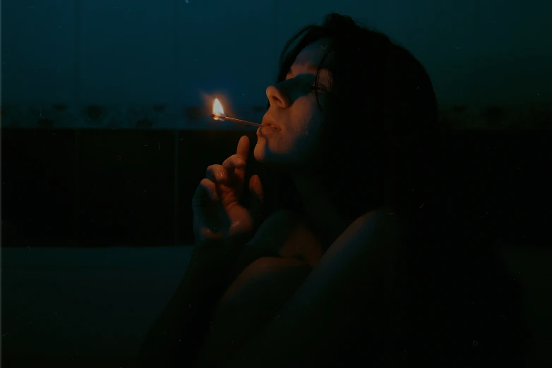 a man sitting down smoking a cigarette in the dark