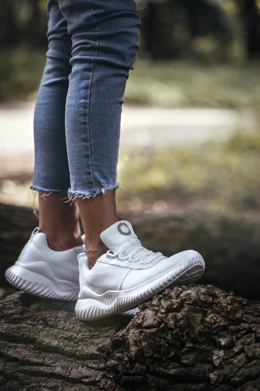 someones white shoes and jeans stand on a log in the woods