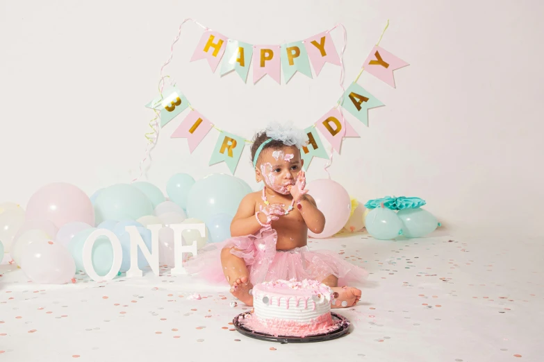 a child sitting in front of a birthday cake with balloons around