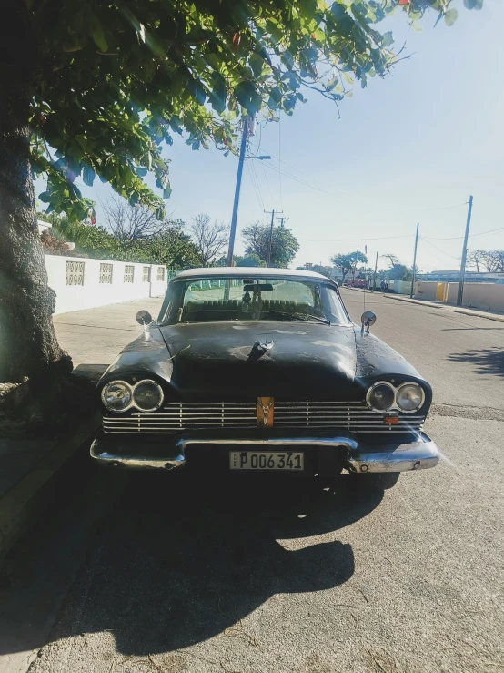 a black car sitting next to a tree on the road