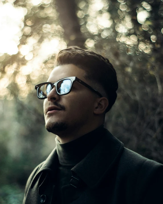 a man wearing sunglasses standing near a forest