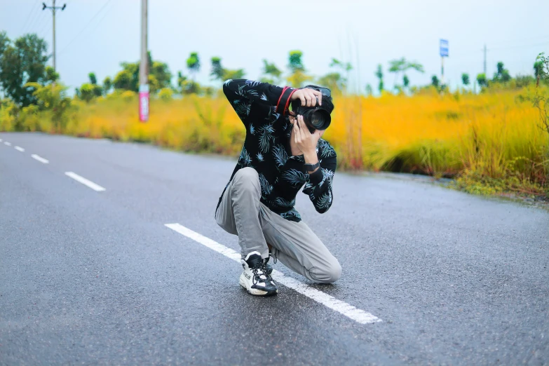 a man crouching in the road while using his cell phone