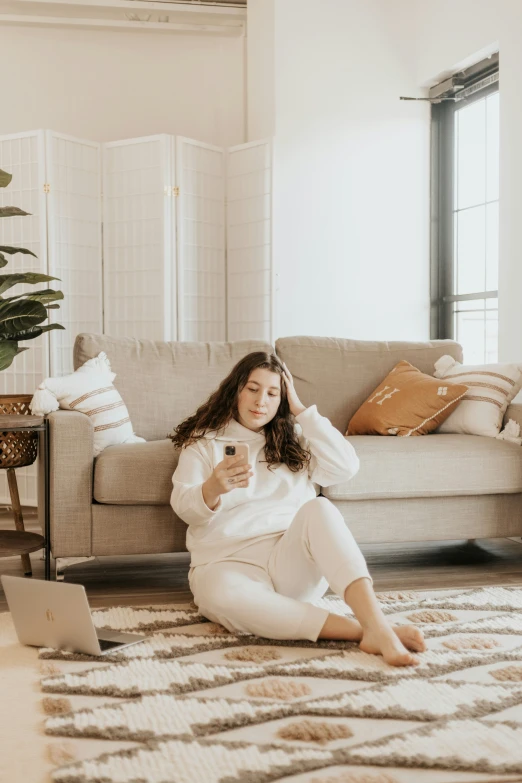 a woman sitting on the floor next to a couch in front of a laptop