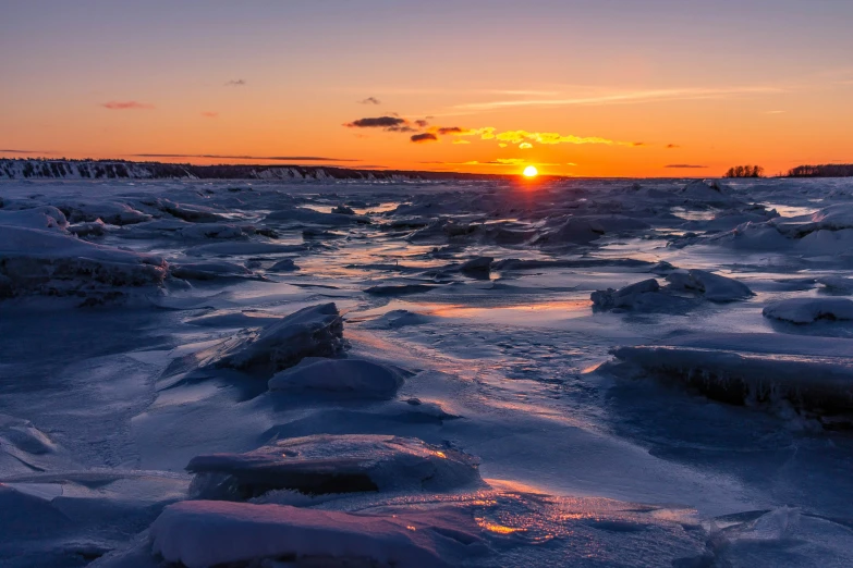 a sunset in the distance over ice covered water