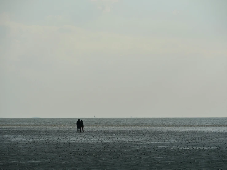 two people standing in the distance on the beach