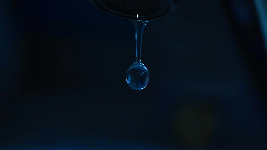 water drop falling onto black surface in a dark room