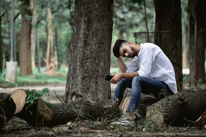 the bearded man sitting on logs is taking a po