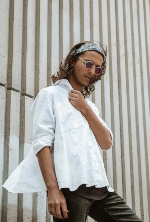 a woman wearing sunglasses and a scarf is posing in front of a corrugated wall