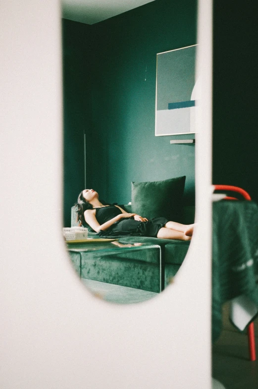 a girl sits on a couch, facing the opposite direction of her reflection