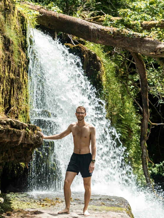 a man is posing in front of a waterfall