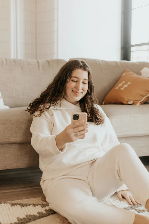 a girl in pyjamas is sitting on a rug looking at her phone