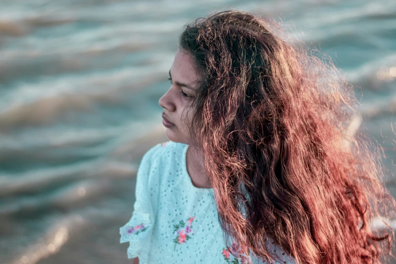 the girl looks at the ocean while holding her hair back