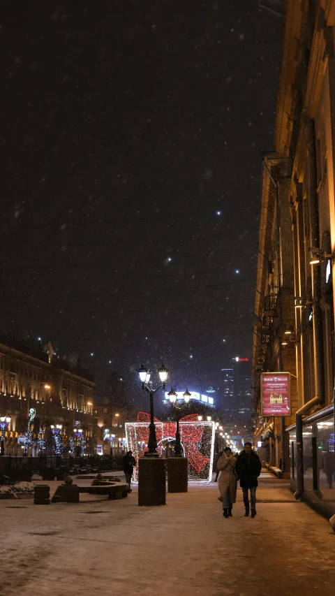 a couple walks down the street near christmas lights