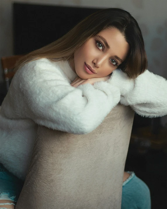 a woman sits in an upholstered chair, with a hand on her neck