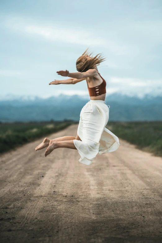 the woman is jumping in the air on a dirt road