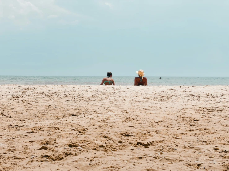 two people are sitting on the beach and one is walking