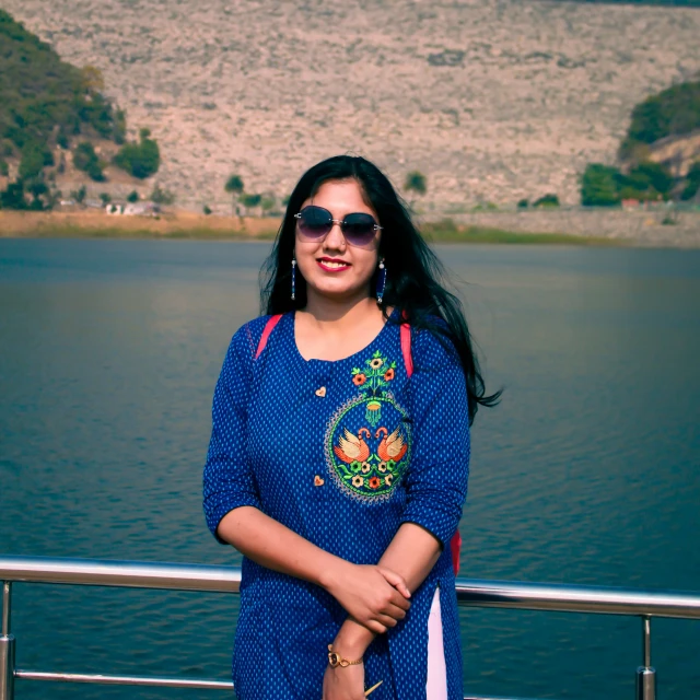 woman wearing blue top near water with mountains behind her