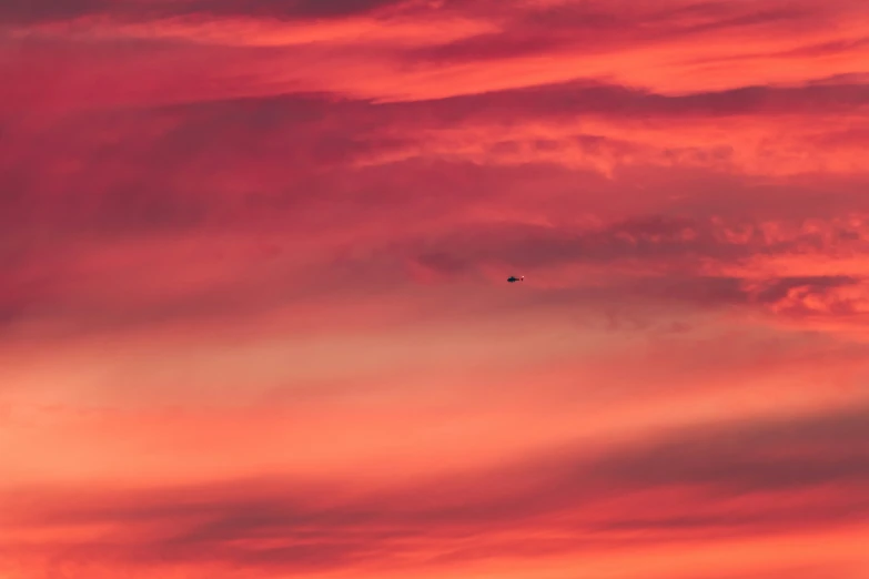 a pink and red sky at sunset with a plane flying in the middle of it